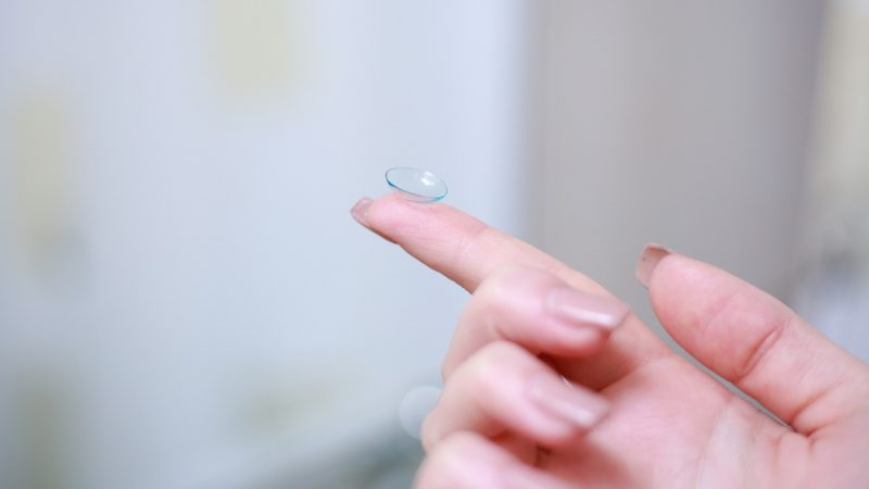 Mulher segura uma lente de contato multifocal na ponta do dedo
