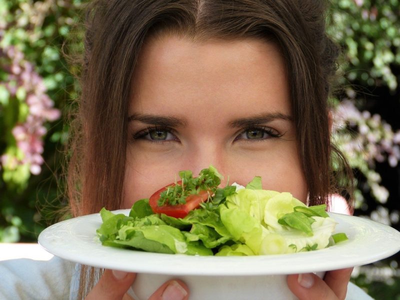 Mulher olha prato de comida cheio de saladas e alimentos bons para os olhos