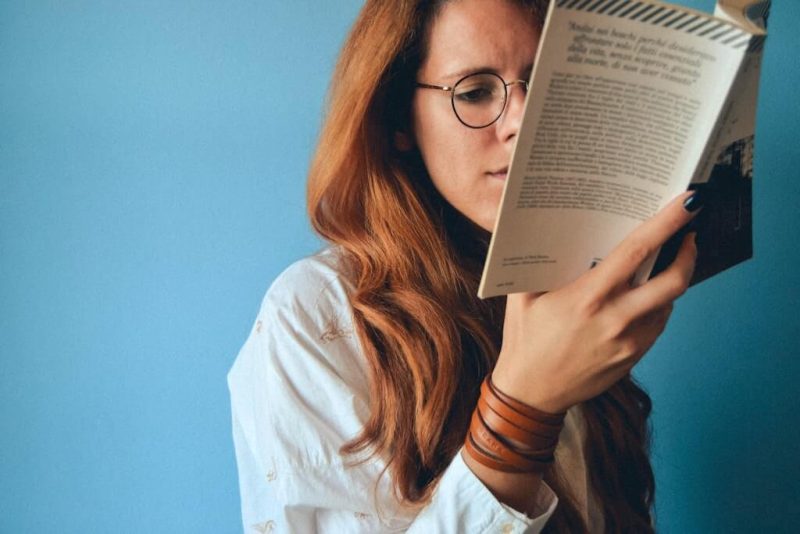 Mulher ruiva usa óculos para perto para ler livro