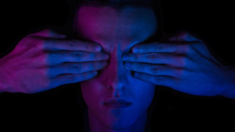 Pessoa com as mãos cobrindo os olhos em uma imagem em tons de azul e roxo representa o daltonismo