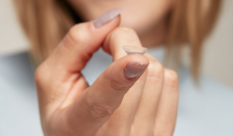 mulher segura lentes de contato na ponta do dedo indicador
